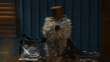 a stuffed animal wearing a top hat and glasses is holding a glass of whiskey
