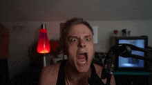 a man screams into a microphone in front of a lava lamp