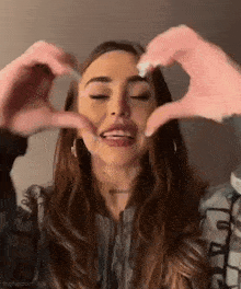 a woman is making a heart shape with her hands and smiling .