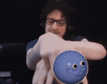 a man with glasses holds a blue ball with a face drawn on it