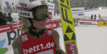 a person wearing a uvex helmet and goggles stands in front of a sign that says bett1.de