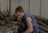 a man in a blue shirt is kneeling down next to a pile of logs