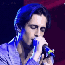 a young man is singing into a microphone while wearing a plaid shirt .
