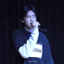a young man singing into a microphone with a tag that says tatchai on it