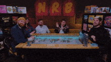 a group of men are sitting around a table with nrb written on a wall behind them