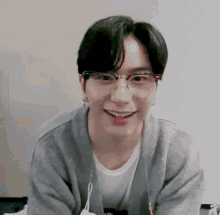 a young man wearing glasses and a gray sweater smiles