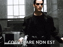 a man in a black coat and sunglasses is holding a gun and saying cochleare non est .