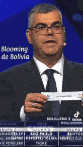 a man in a suit and tie is holding a piece of paper that says ' blooming de bolivia ' on it