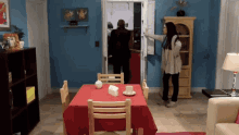a woman opens a door to a room with a red table cloth