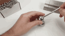 a person is holding a metal ball with a screwdriver in front of a box of metal balls