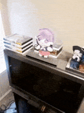 a stuffed animal sits on top of a stack of dvds on a tv stand