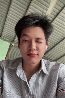 a young man wearing a striped shirt and ear buds winks at the camera