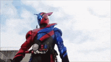 a red and blue kamen rider is standing in front of a blue sky .