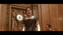 a woman in a dress stands in front of a clock that shows the time as 4:20