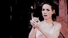 a woman in a white tank top is holding a cell phone in her hand