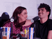 a man and a woman sit in front of microphones that say eh on them