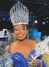 a drag queen is wearing a crown and holding a trophy in front of a drag source logo
