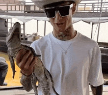a man wearing sunglasses and a cowboy hat is holding a small alligator .