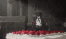 a man is sitting in front of a large cake with red frosting in a dark room .