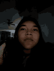 a girl taking a selfie in a dark room with a ceiling fan