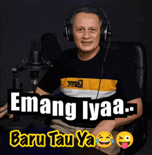 a man wearing headphones sits in front of a microphone with the words emang lyaa baru tau ya written below him