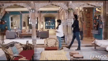 a man and a woman are walking in a living room with a lot of furniture .