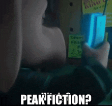 a person is holding a cell phone in front of a sign that says peak fiction