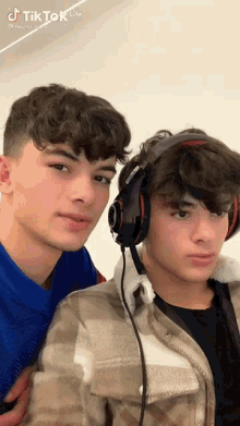 two boys wearing headphones are standing next to each other and looking at the camera .