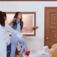 two women are having a pillow fight in a room with a window .