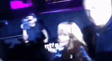 a man and a woman are standing on a stage in a dark room with purple lights .