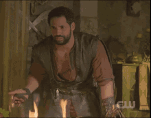 a man sitting in front of a fire with a cw logo on the bottom right