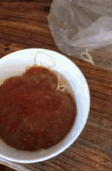 a white bowl filled with spaghetti and tomato sauce on a wooden table