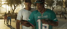 a man wearing a manatees jersey looks at a phone