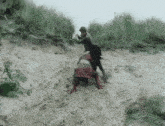 a man and a woman are playing in the sand on a hillside