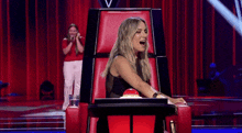 a woman sits in a chair with her mouth open and a red button on it