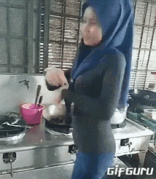 a woman wearing a blue hijab is standing in a kitchen preparing food .