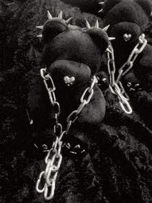 a black teddy bear with spikes on its head is chained to a chain