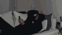 a man in a black hoodie is laying on a couch looking at his cell phone .