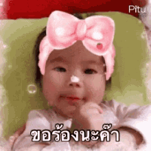 a baby wearing a pink headband with a bow on it is laying on a pillow .