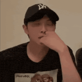 a man wearing a baseball cap and a t-shirt is covering his nose with his hand .