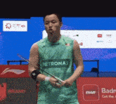 a man is holding a badminton racket and wearing a petronas shirt