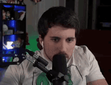 a man wearing a white shirt with a green frog on it is talking into a microphone ..