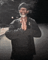 a man with a beard is standing with his hands folded in front of his face .