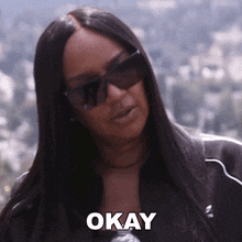 a woman wearing sunglasses says okay in front of her face