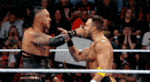 two wrestlers are wrestling in a ring and one of them is slapping the other on the face .