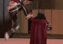 a man in a red cape is kicking another man in a white costume