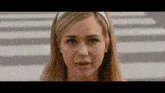 a woman wearing a white headband and earrings looks at the camera