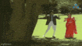 a man in a suit and a woman in a red dress are dancing in a park .