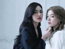 two women are standing next to each other with one touching the other 's face
