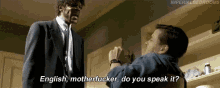 a man in a suit and tie is talking to another man in a blue shirt who is asking him if he speaks english